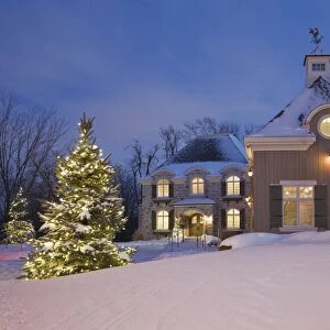 Luxurious residential cottage style home with illuminated evergreen trees at dusk in winter, Quebec, Canada