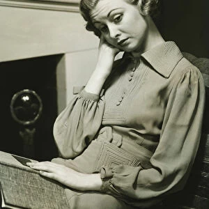 Pensive woman sitting by fireplace with book on laps, (B&W)