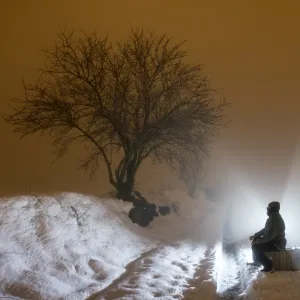 Silhouette of a person sitting on a suitcase resting, for a covered way of snow and fog during the night