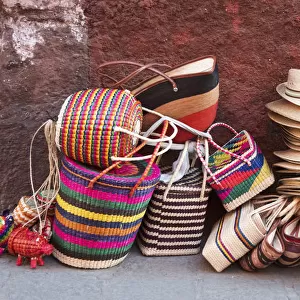 Woven souvenirs on display on a sidewalk against a wall