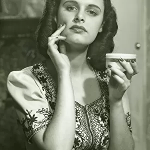 Young woman applying creme on face, (B&W), portrait