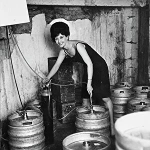 Glamour in the cellar as barmaid Lois taps another barrel of beer. 19 October 1963