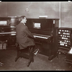 A man playing a player piano in a piano showroom in New York, 1907 (silver gelatin print)