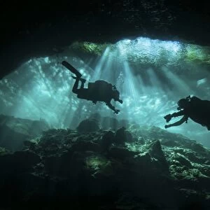 Two divers silhouetted in light at entrance to Chac Mool cenote, Mexico