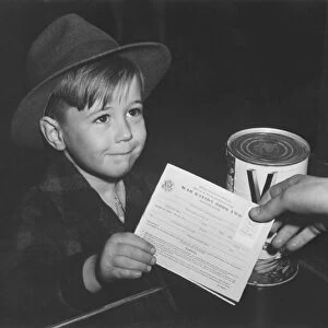 An eager school boy gets his first experience in using War Ration Book Two. circa 1943
