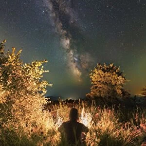 Man sitting near the campfire in the forest under the stars and Milky Way, Sudak, Crimea