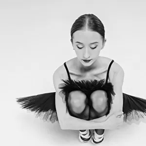 a portrait of a ballerina in a black tutu squatting hugging her knees