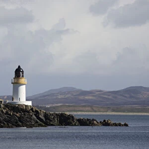 Lighthouse At The Waters Edge Under A Cloudy Sky; Port Charlotte, Isle Of Islay, Scotland