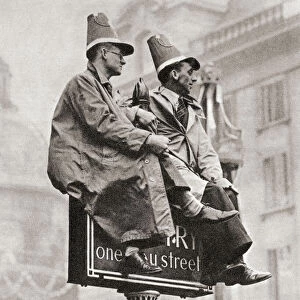 Two men atop a traffic sign in order to get a better view of the Coronation procession of George VI and Queen Elizabeth, London, England, 1937. From The Coronation in Pictures, published 1937