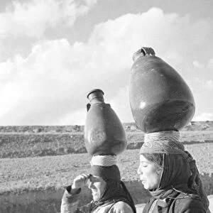 Two Arab women carrying water jars on their head on the Jerusalem road in Palestine