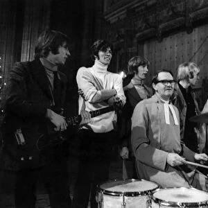 The Bee Gees pop group stand behind a vicar having a a go on the drums during rehearsals