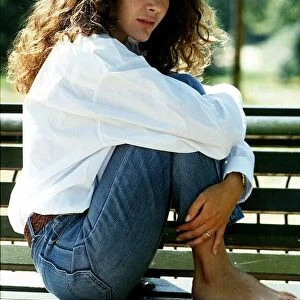 Laurence Ashley a French actress sitting sideways on a park bench with her feet up