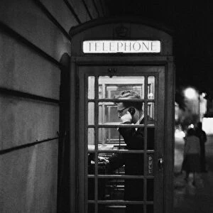 A man making a call from a public telephone box in London. 31st August 1958