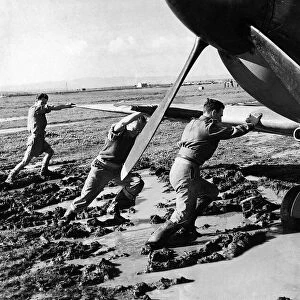 An RAF ground crew pushes a Supermarine Spitfire out of the mud on a boggy