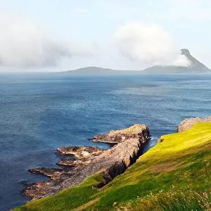 Morning view onto the Faroese island Koltur with spectacular clouds and blue water in a dramatic valley with mountain range. Faroe Islands, Denmark