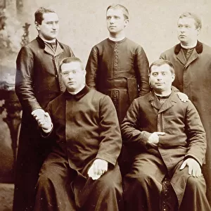 Portrait of a group of priests in their cassocks. Two of them are seated in the foreground, the other three behind them. Two of them are shaking hands