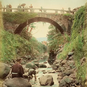 View of Amida Bridge at Nagasaki, with a few people walking across it. In the foreground, two men fishing
