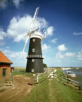 <b class=qtipBold><figcaption>Berney Arms Windmill J850090</figcaption></b><br>BERNEY ARMS WINDMILL, Norfolk Broads. General view with river and boats. One of Norfolk's best and largest extant marsh mills, built to grind a constituent of cement and in use until 1951, finally pumping water to drain surrounding marshland.<br><em>© Historic England</em> Berney Arms Windmill J850090