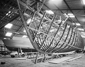<b class=qtipBold><figcaption>Boatyard, Norfolk BB99_01083</figcaption></b><br>F B Wild's Boatyard, Horning, Norfolk. Interior view. Two boats at different stages of construction, and a parked moped. Photographed by Hallam Ashley 1963.<br><em>© Historic England</em> Boatyard, Norfolk BB99_01083