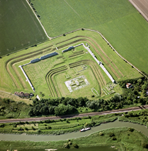 <b class=qtipBold><figcaption>Richborough Roman Fort N070696</figcaption></b><br>RICHBOROUGH ROMAN FORT, Sandwich, Kent. Aerial view. Richborough, or 'Rutupiae' was known to be a major naval base This shows the triple ditch defences of the early 3rd century fort surrounding the concrete base of the 1st century monumental arch. All of these are surrounded by the outer defensive wall of a Saxon Shore fort - the bases of the 'Classis Britannica' the Roman fleet based around the coast of Britain.<br><em>© Historic England</em> Richborough Roman Fort N070696