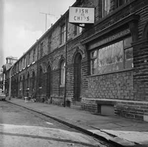 <b class=qtipBold><figcaption>Saltaire DES01_01_0626</figcaption></b><br>Looking east along Titus Street, Saltaire, Shipley, Bradford, showing houses on the south side of the street with the Titus Street Fisheries at 39 Titus Street in the foreground. Photographed by Eileen Deste between 1966 and 1974.<br><em>© Historic England Archive</em> Saltaire DES01_01_0626