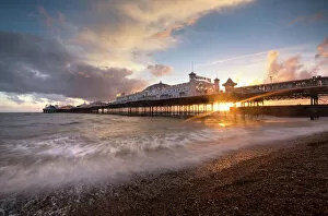 Lens Flare Collection: Brighton Pier at sunset with dramatic sky and waves washing up the beach, Brighton