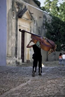 Cobble Collection: Musician carrying double bass along cobbled street to Plaza Mayor, Trinidad