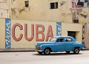 West Indian Gallery: A vintage 1950s American car passing a Viva Cuba sign painted on a wall in cental Havana, Cuba