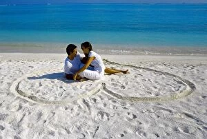 Full Body Collection: Young couple on beach sitting in a heart shaped imprint on the sand, Maldives