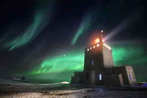 Dyrholaey lighthouse in winter with aurora borealis dancing above it, Sudurland, Iceland Dyrholaey lighthouse in winter with aurora borealis dancing above it, Sudurland, Iceland