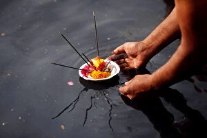 Oil Lamp Collection: A man places an oil lamp in the polluted river Yamuna after offering prayers