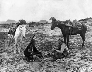 Seated Gallery: PLAYING CARDS, c1915. A cowboy and a Native American man seated on a blanket
