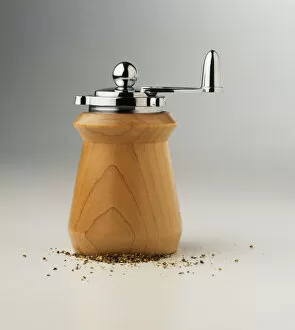 Wooden pepper grinder with stainless steel handle, and crushed peppercorns at base